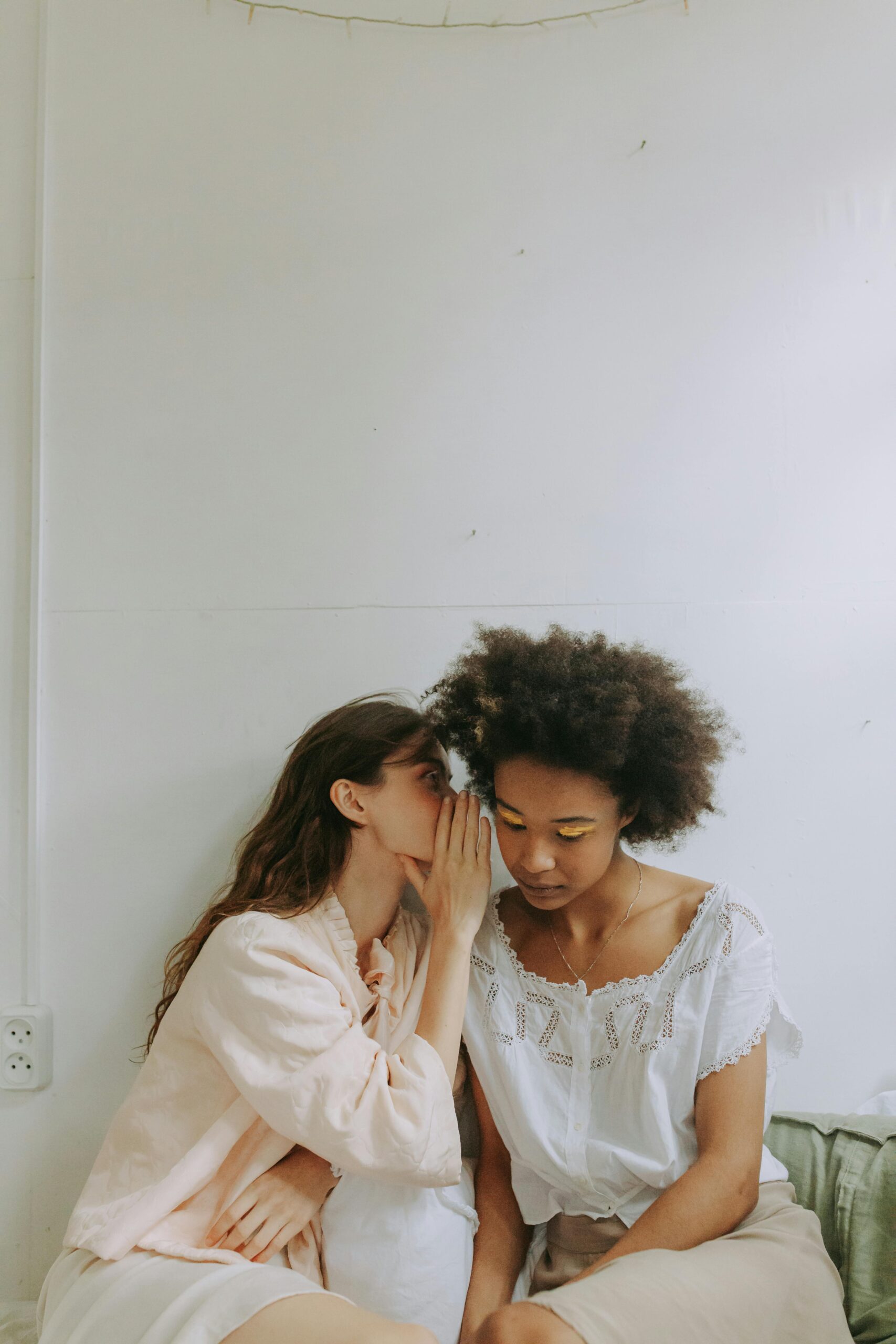 How to find the one - Two women sitting on a bed, engaged in conversation and sharing a secret with one another.