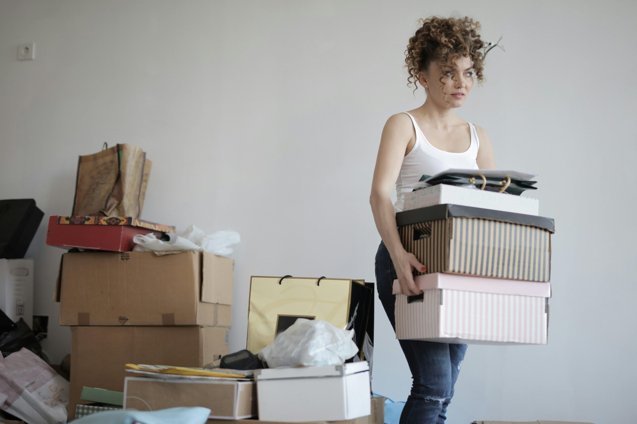 Life transitions - In a room packed with boxes, a woman stands while carrying a few boxes in her hands.