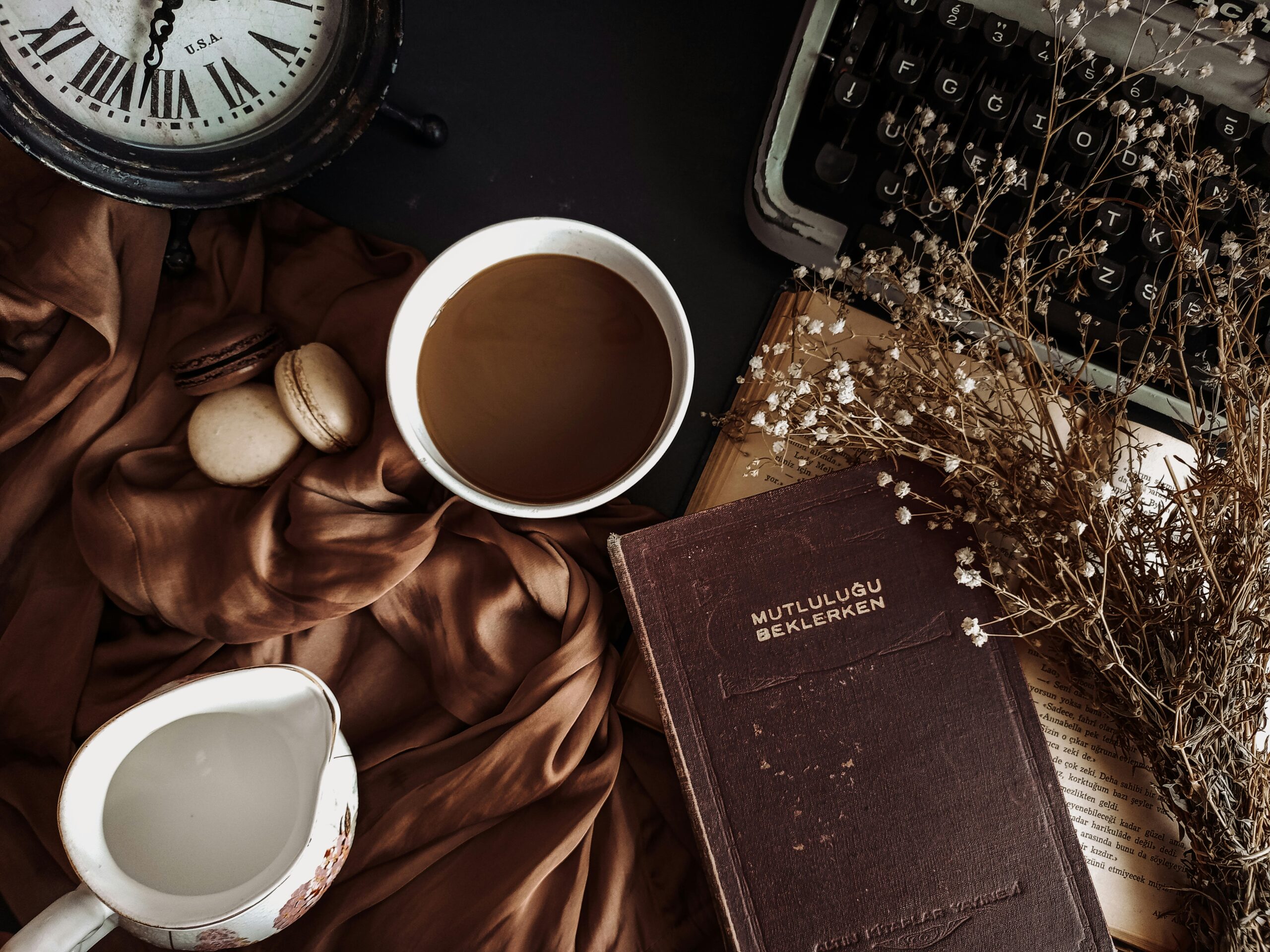 aesthetic quotes - A table setting with a book, coffee, and clock, along with a typewriter, creamer, and silk sheet.