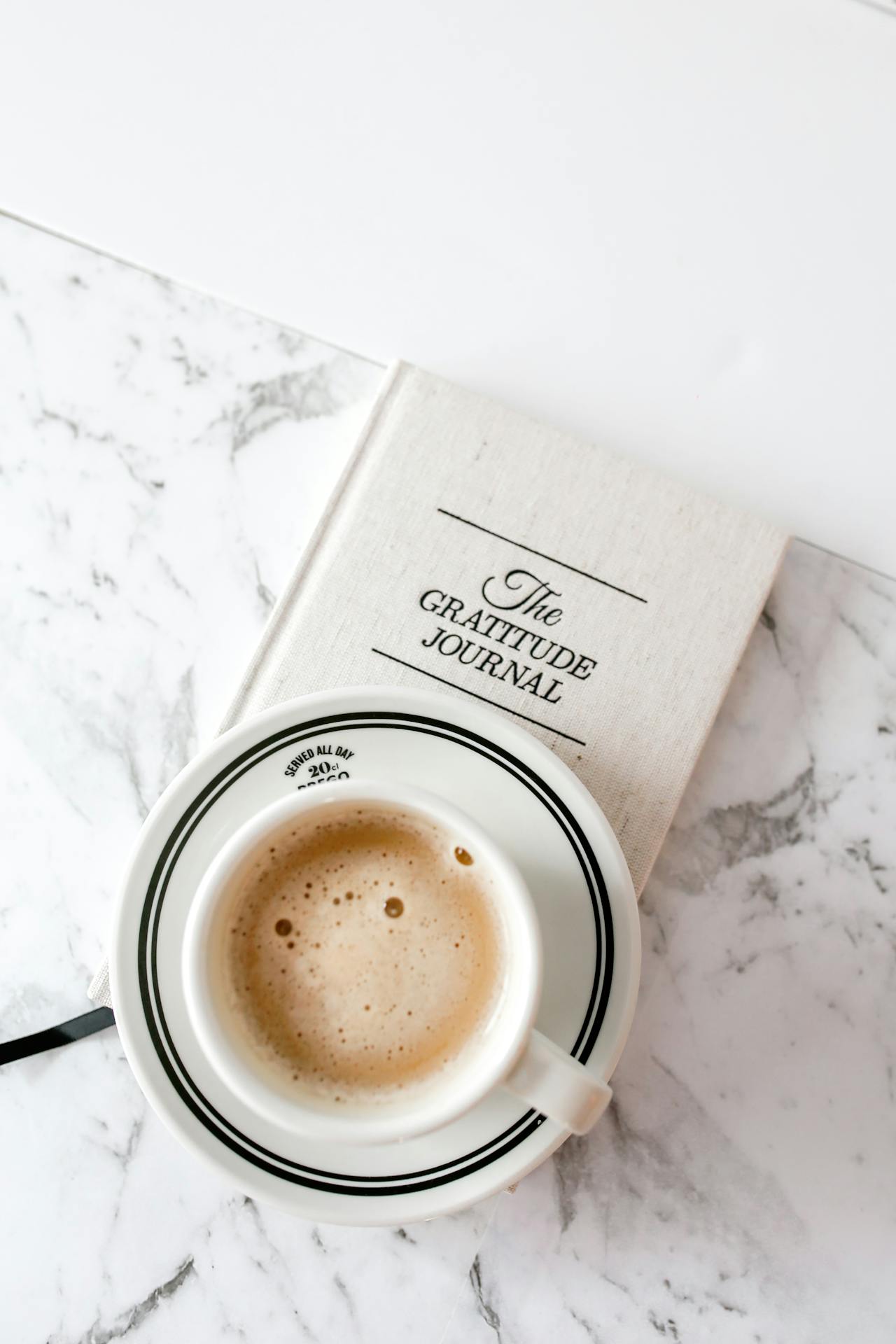 Types of journaling: cup of coffee sitting on top of a notebook titled "the gratitude journal" on a white, marbled surface