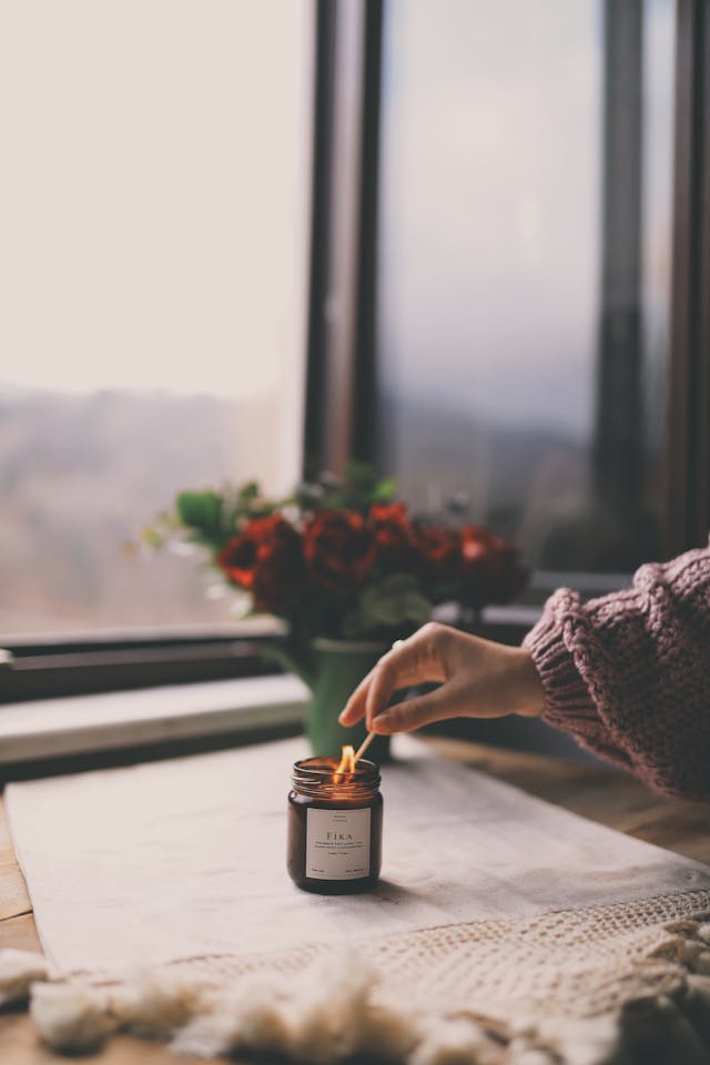 get cozy - person lighting a candle with a match near a window