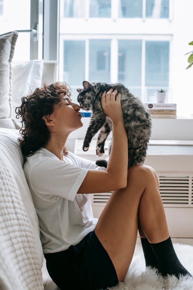 get cozy - woman sitting on the floor next to a bed holding a black and white cat