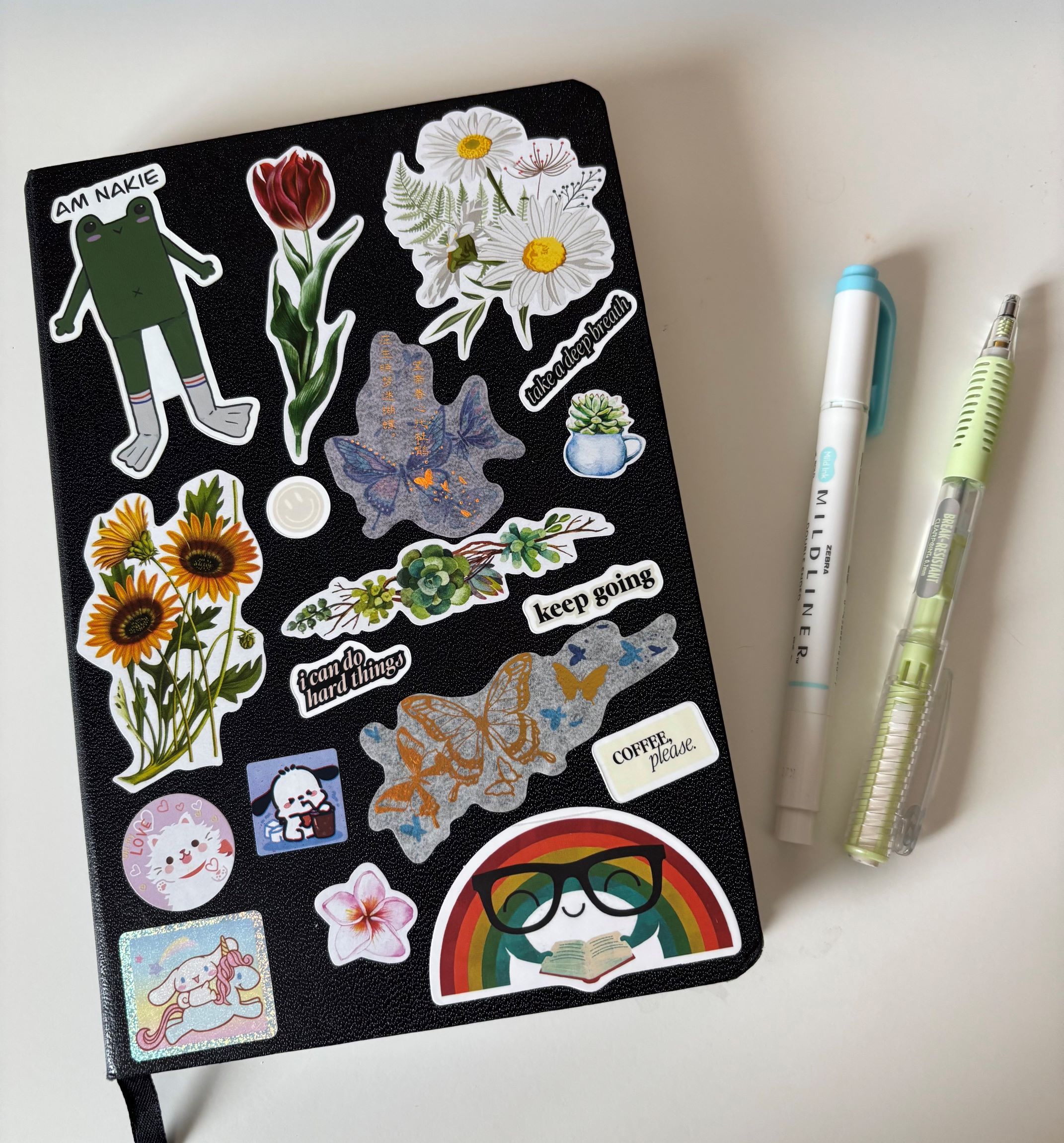 my black journal with lots of floral and other stickers next two a marker and a pencil