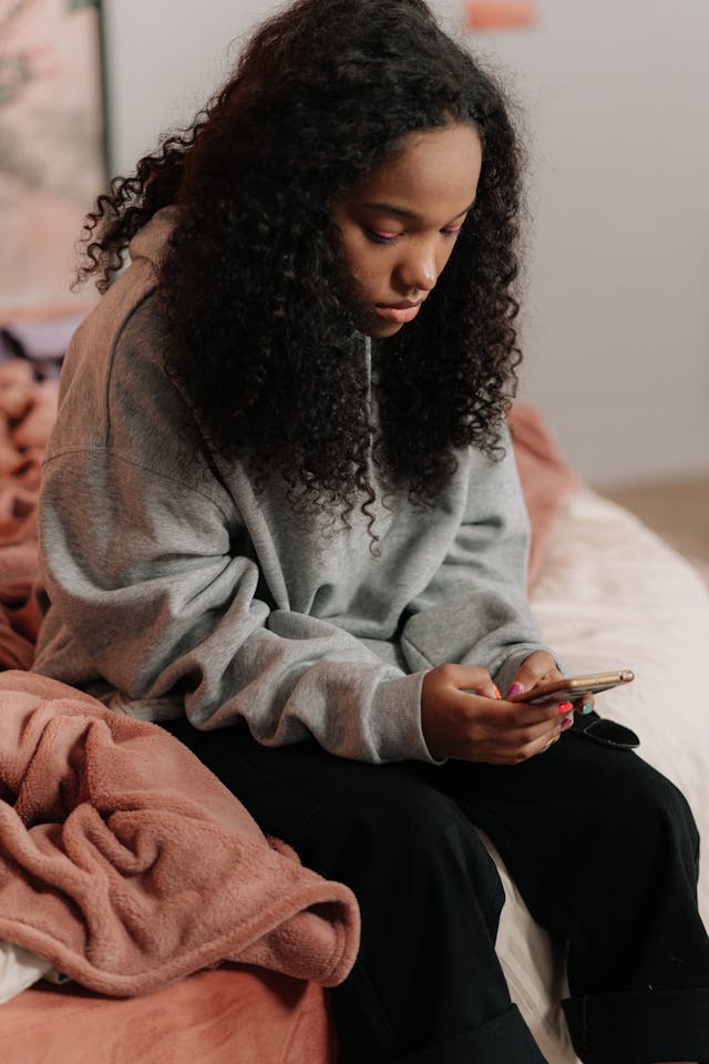 woman sitting on edge of bed using smartphone