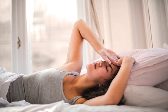 woman laying in bed with the back of her hand across her forehead, softly smiling